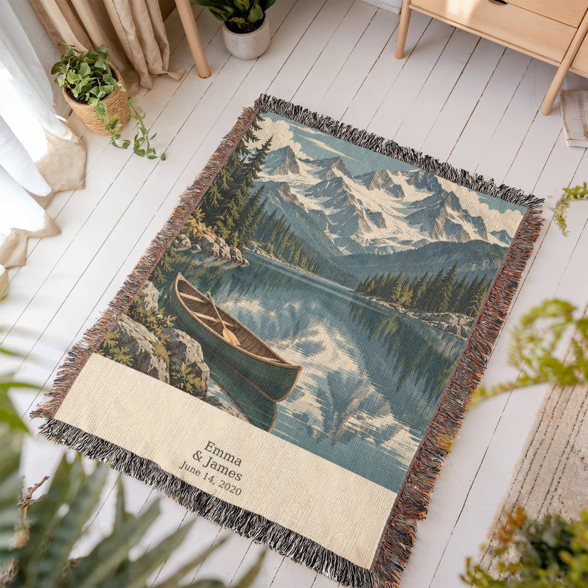 Mountain Lake personalized woven blanket laid flat on a white wooden floor in a bright room, mountains, lake and canoe above "Emma & James" and June 14, 2020.