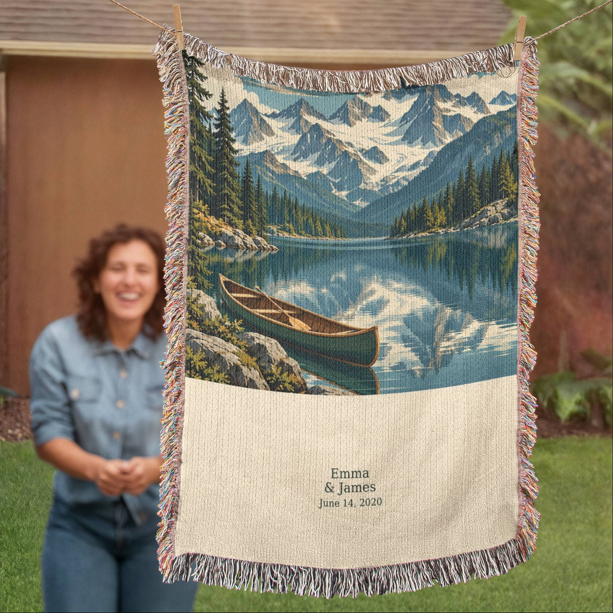 Mountain Lake personalized woven blanket hung outdoors beside a smiling woman, showing the full design with "Emma & James" and June 14, 2020.
