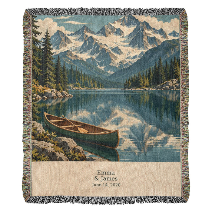 Mountain Lake personalized woven cotton blanket shown full front: snowy peaks, pines and a green canoe on a mirrored lake, with the woven names and date on the cream panel.