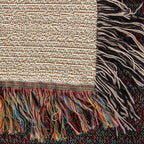 Corner close-up of the Mountain Lake woven cotton blanket showing the cream cotton weave, the multicolour bottom fringe and the black-and-white side fringe.