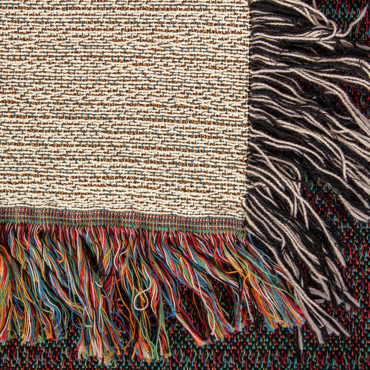 Corner close-up of the Mountain Lake woven cotton blanket showing the cream cotton weave, the multicolour bottom fringe and the black-and-white side fringe.