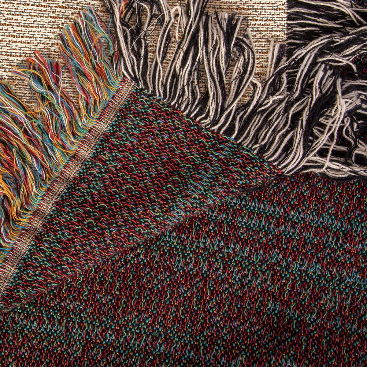 The Mountain Lake woven cotton blanket folded back at the corner to show the reverse weave and the colourful fringe along the hem.