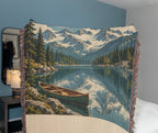 Mountain Lake woven cotton blanket draped in a cosy bedroom, the woven mountains, lake reflection and canoe artwork in full view.