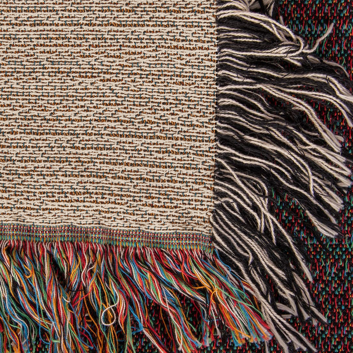 Corner close-up of the Coastal woven cotton blanket showing the cream cotton weave, the multicolour bottom fringe and the black-and-white side fringe.