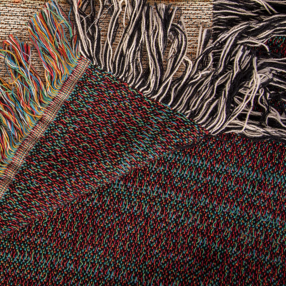 The Coastal woven cotton blanket folded back at the corner to show the reverse weave and the colourful fringe along the hem.
