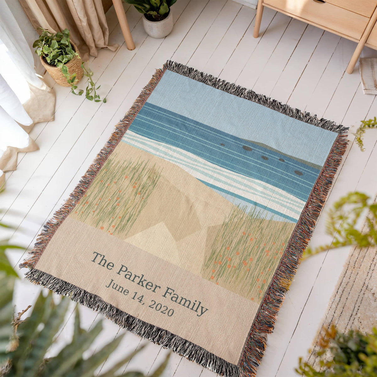 Coastal personalized woven cotton blanket laid flat on a white wooden floor in a sunny room, showing the whole design and fringe.