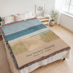 Coastal personalized woven cotton blanket spread across a bed in a bright bedroom, seen at an angle with the whole blanket in frame.