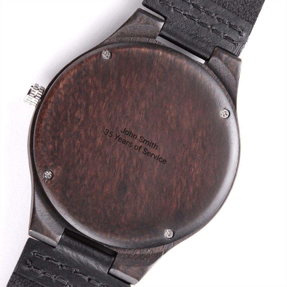 Close-up of the back of a dark wooden watch with black leather strap, caseback engraved "John Smith 35 Years of Service"