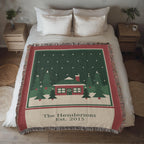 Personalized family name Christmas woven cotton blanket spread on a bed, showing the red cabin, evergreens, family name and year with fringe