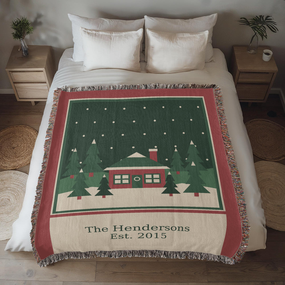 Personalized family name Christmas woven cotton blanket spread on a bed, showing the red cabin, evergreens, family name and year with fringe