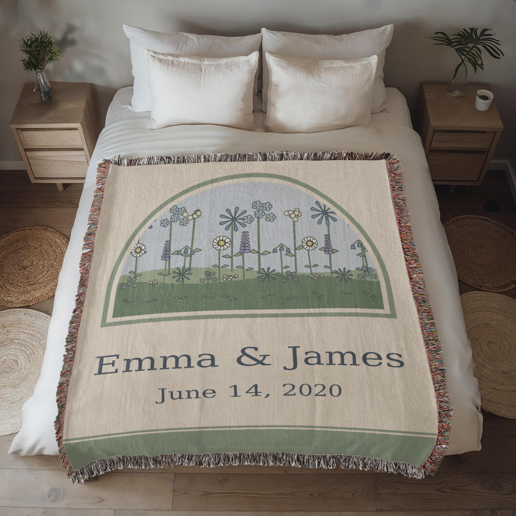 Wildflower anniversary woven blanket spread across a made bed, soft blue and sage meadow arch with couple names and wedding date