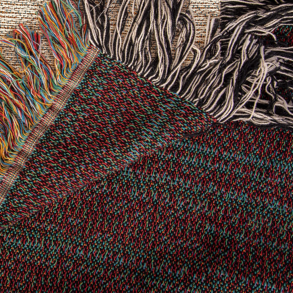 The Cabin woven cotton blanket folded back at the corner to show the reverse weave and the colourful fringe along the hem.