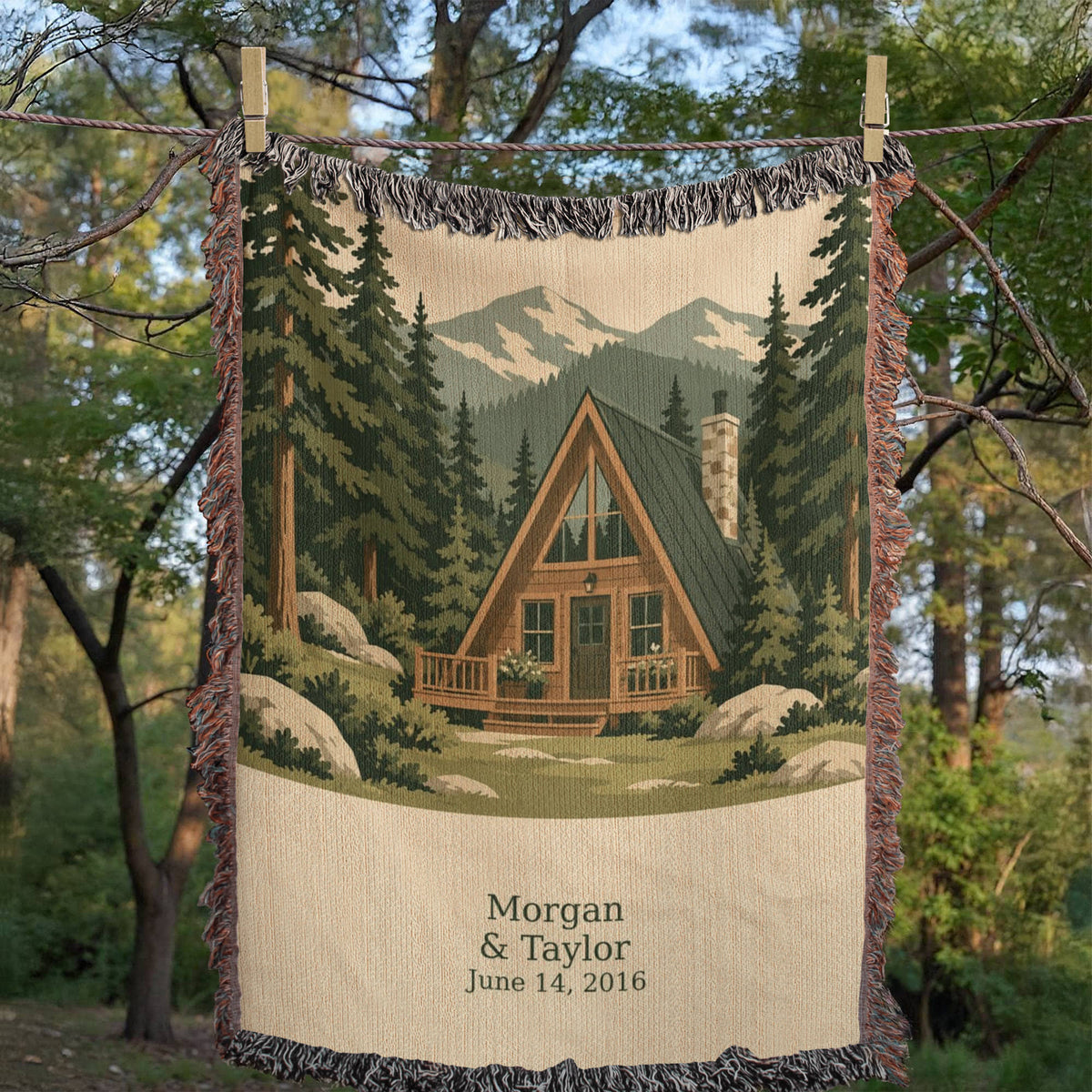 Cabin personalized woven cotton blanket hung on an outdoor line among trees, the whole front in view with the woven cabin scene and lettering panel.