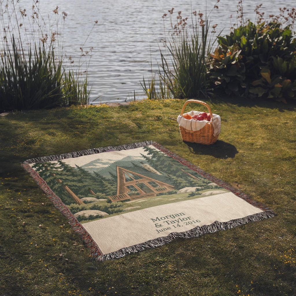 Cabin personalized woven cotton blanket spread on lakeside grass beside a picnic basket, the whole blanket in view.