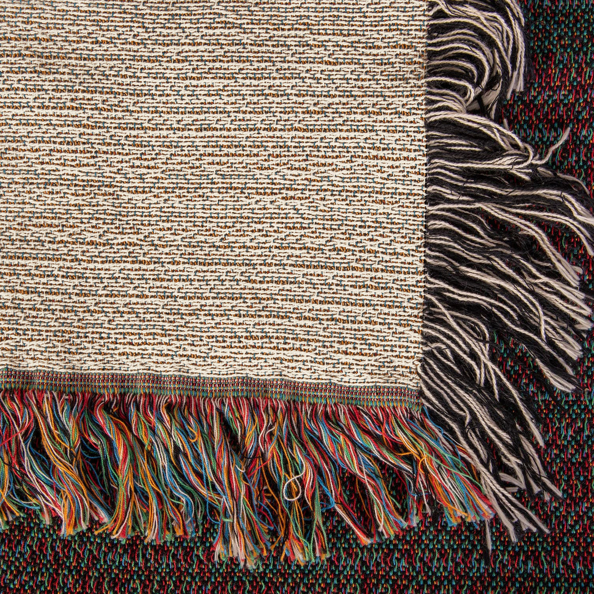 Corner close-up of the Cabin woven cotton blanket showing the cream cotton weave, the multicolour fringe along the bottom edge and the black-and-white side fringe.