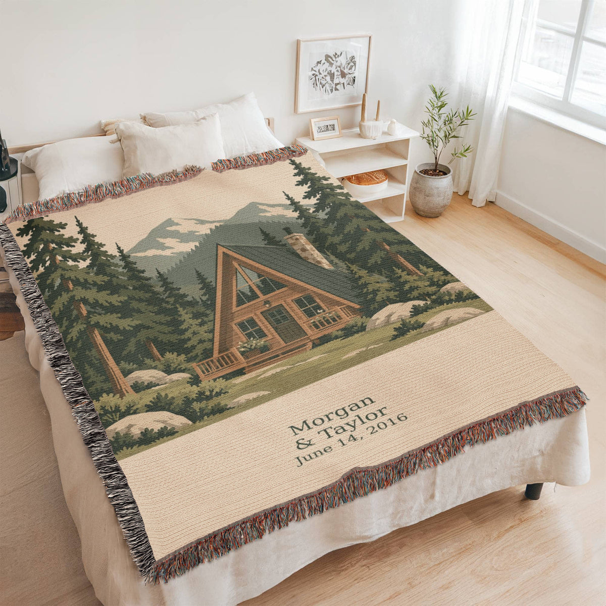 Cabin personalized woven cotton blanket spread across a bed in a bright bedroom, seen at an angle with the whole blanket in frame.