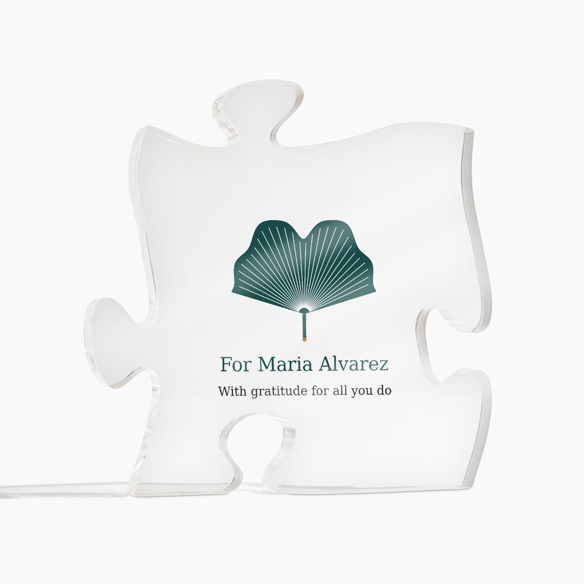 Clear acrylic puzzle-piece caregiver plaque on a white background, printed with a green design and the text "For Maria Alvarez" and "With gratitude for all you do"