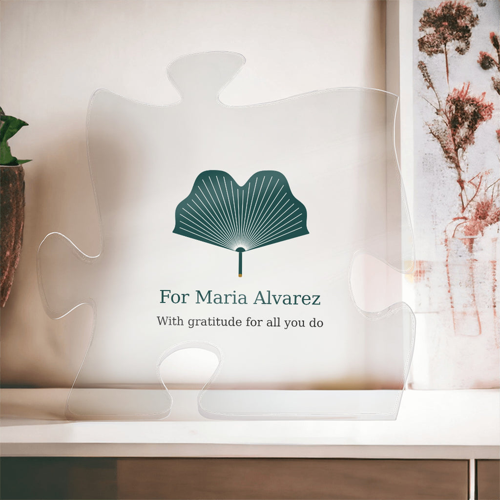 Clear acrylic puzzle-piece caregiver plaque in front of a window with dried flowers, with the text "For Maria Alvarez" and "With gratitude for all you do"
