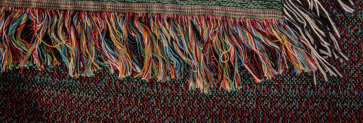 Corner of the Tiger Botanical woven cotton blanket showing the multicolor bottom fringe meeting the black-and-white side fringe.