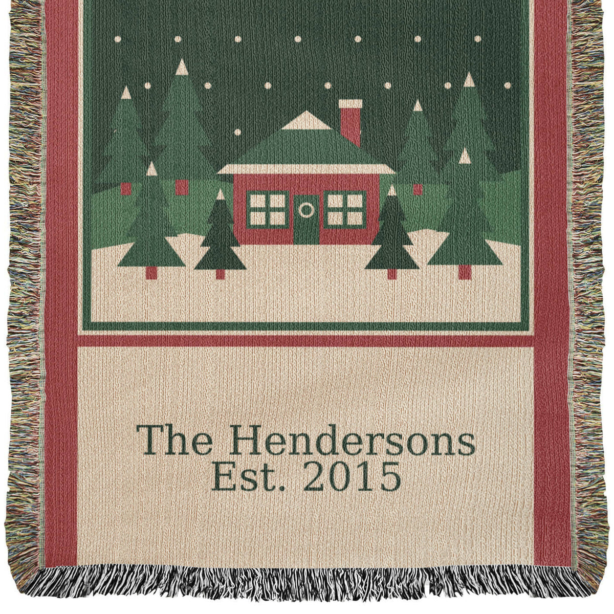 Close view of the personalized family name Christmas woven blanket: red cabin, evergreens and snow above the woven family name and year