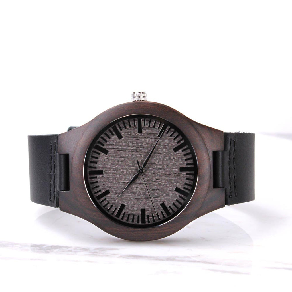 Front view of a dark wooden watch with a black leather strap on a white background