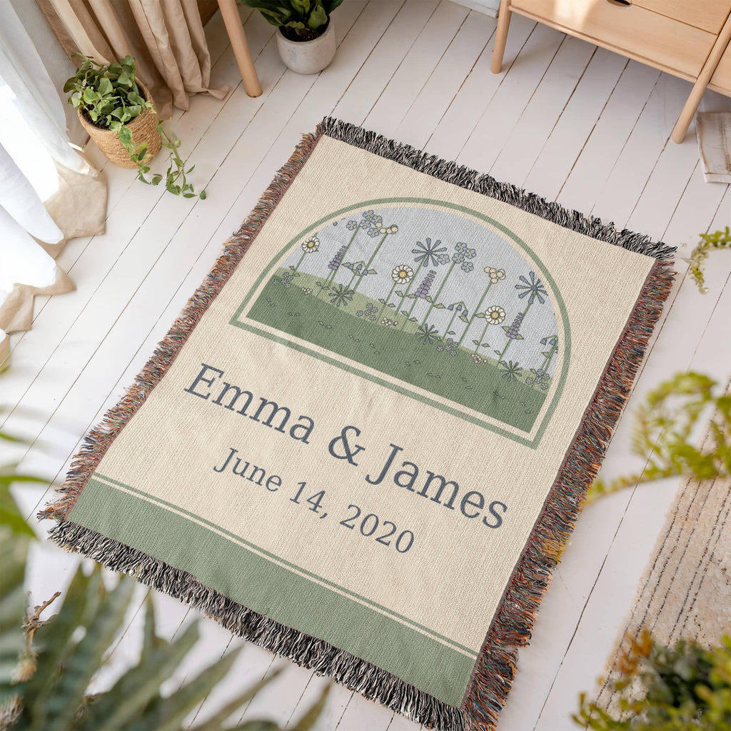 Wildflower anniversary woven cotton throw laid on a light wood floor, arched meadow of cornflowers and daisies over the couple names and date