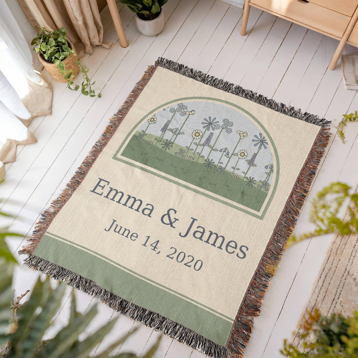 Wildflower anniversary woven cotton throw laid on a light wood floor, arched meadow of cornflowers and daisies over the couple names and date