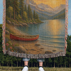 Be Still lake woven throw held up outdoors in a field, red canoe and fringe in view with only feet below