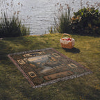 Moose and bear woven cotton throw laid on the grass beside a lake with a picnic basket, fringed edges on all sides