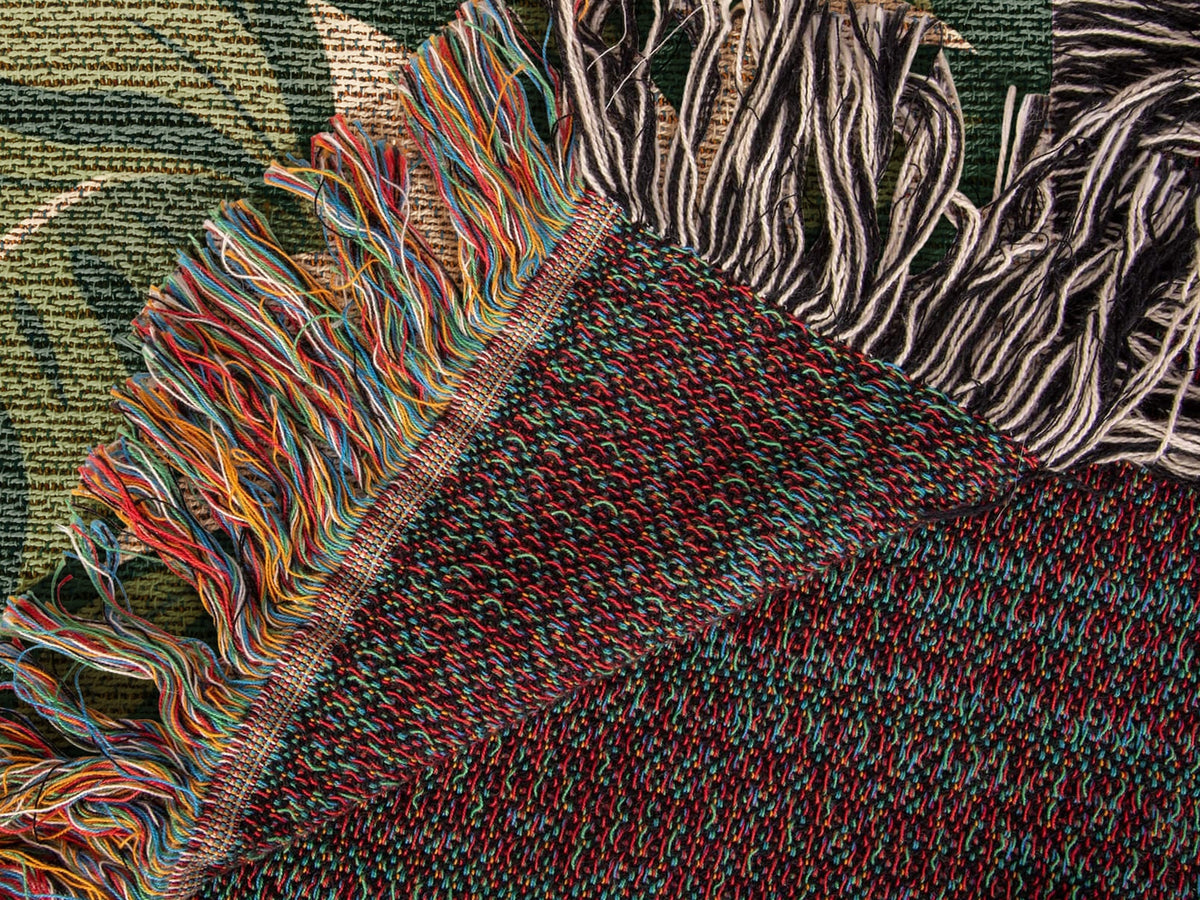 Folded corner of the Tiger Botanical woven cotton blanket showing the diagonal fold, stitched hem, both fringes and the woven reverse side.