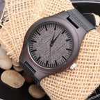 Front view of a dark wooden watch with a black leather strap on burlap with stones