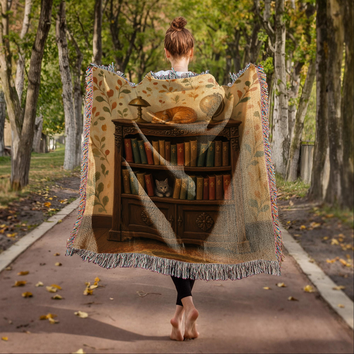 Library cat woven throw: orange tabby folk art worn as a wrap on a tree-lined path, seen from behind, fringe on all edges