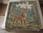Closer view of the Forest Stag woven cotton blanket laid on a bed: the whole stag with full antlers and legs, the woven forest scene and fringe.