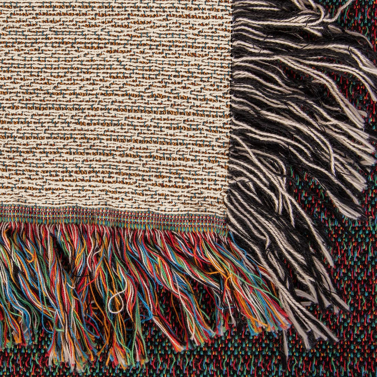 Corner close-up of the Family Caravan woven cotton blanket showing the cream cotton weave, the multicolour bottom fringe and the black-and-white side fringe.
