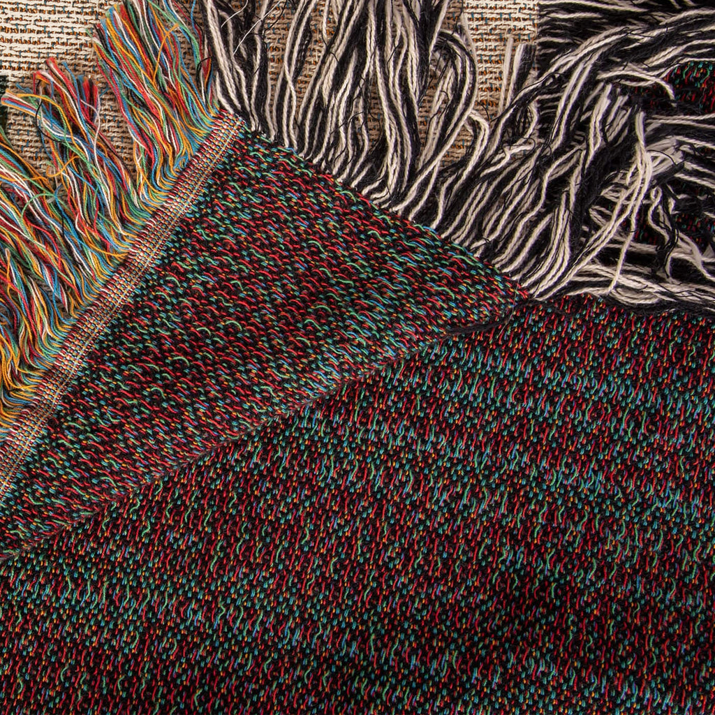 The Family Caravan woven cotton blanket folded back at the corner to show the reverse weave and the colourful fringe along the hem.