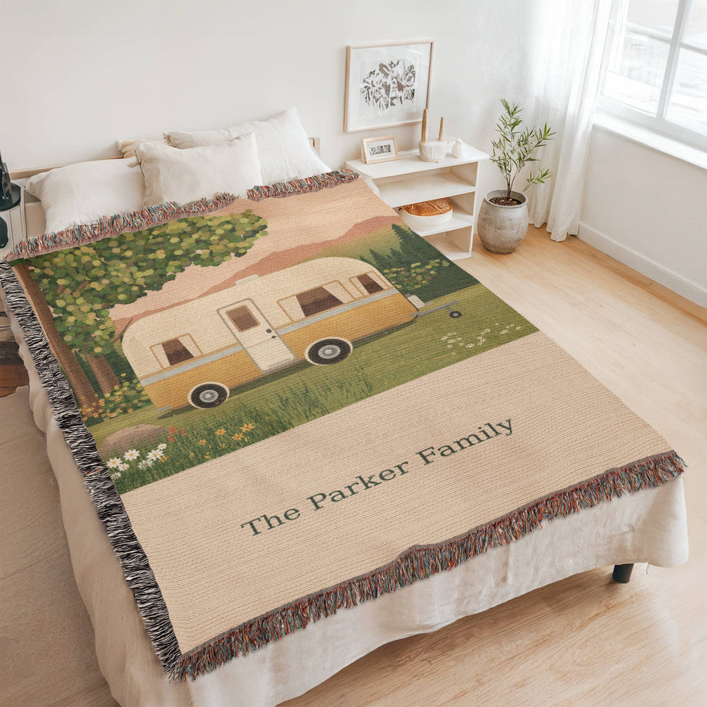 Family Caravan personalized woven cotton blanket spread across a bed in a bright bedroom, seen at an angle with the whole blanket in frame.