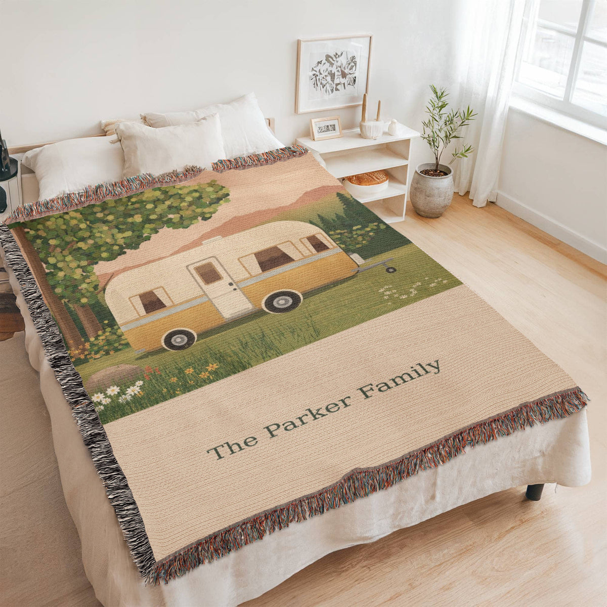 Family Caravan personalized woven cotton blanket spread across a bed in a bright bedroom, seen at an angle with the whole blanket in frame.