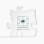 Clear acrylic puzzle-piece coach plaque on a white background, printed with a green design and the text "Coach Daniels" and "Thank you for believing in us"
