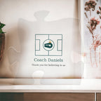 Clear acrylic puzzle-piece coach plaque in front of a window with dried flowers, with the text "Coach Daniels" and "Thank you for believing in us"