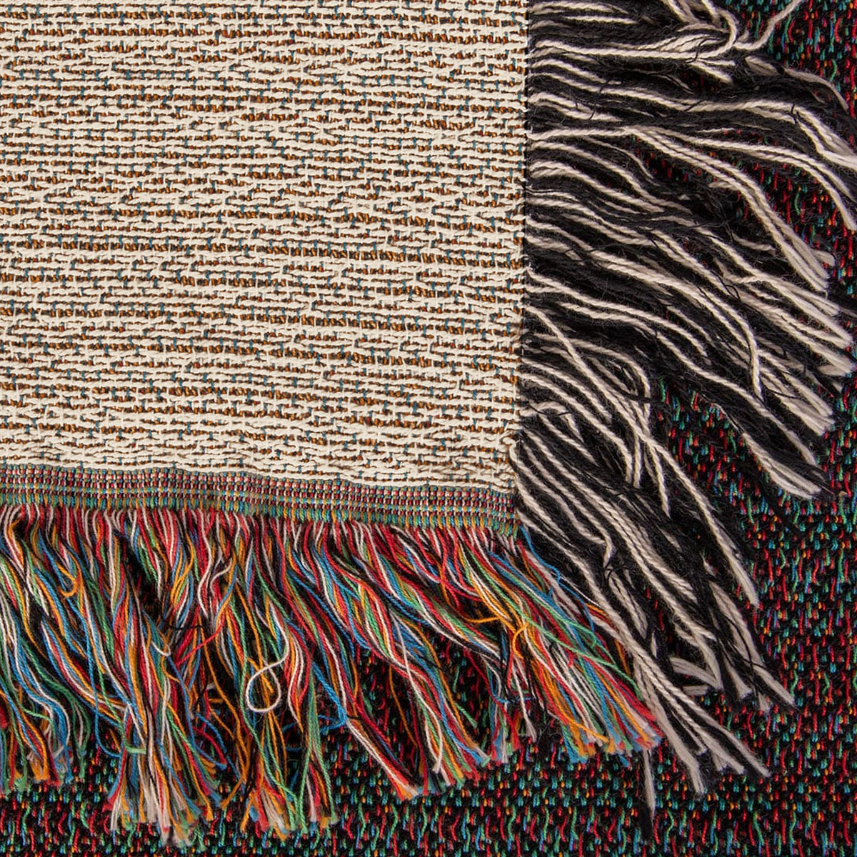 Corner close-up of the Lake House woven cotton blanket showing the cream cotton weave, the multicolour bottom fringe and the black-and-white side fringe.