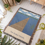 Lake House personalized woven cotton blanket laid flat on a white wooden floor in a sunny room, showing the whole design and fringe.