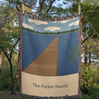 Lake House personalized woven cotton blanket pegged on a clothesline among trees, showing the whole design and the woven names.