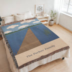 Lake House personalized woven cotton blanket spread across a bed in a bright bedroom, seen at an angle with the whole blanket in frame.