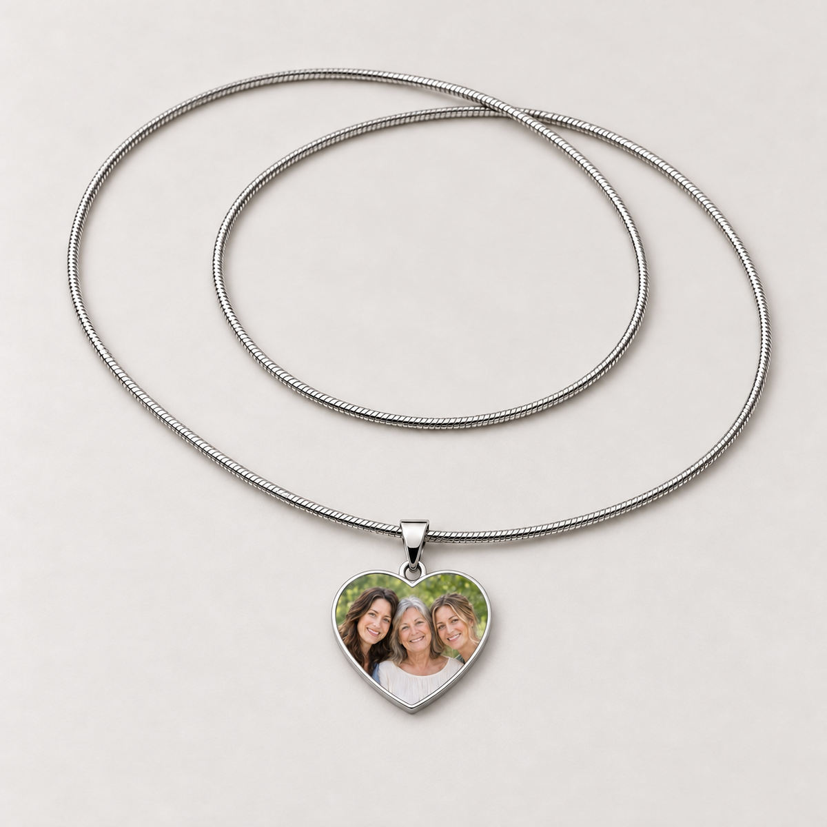 Steel heart photo necklace with a family photo of three smiling women on the pendant and a full snake chain
