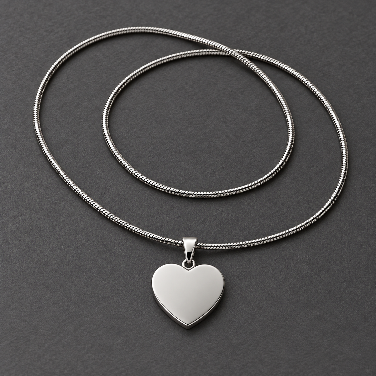 Smooth polished steel back of the heart pendant with the full snake chain on a dark gray surface
