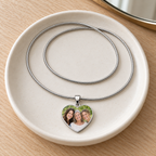 Family photo heart necklace resting on a cream ceramic vanity dish beside a round mirror
