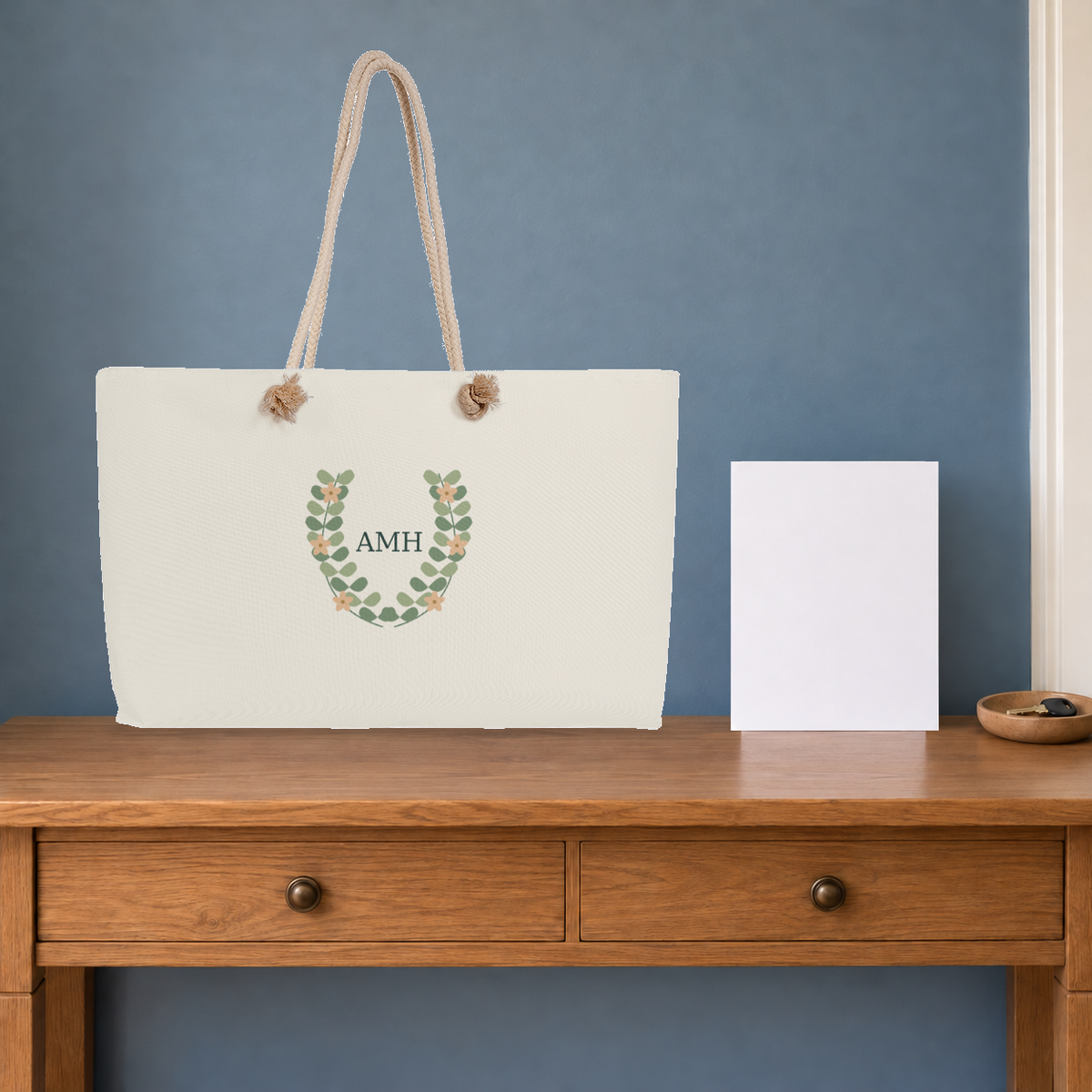 AMH botanical cream-rope weekender on a wooden console in a composed travel setting.