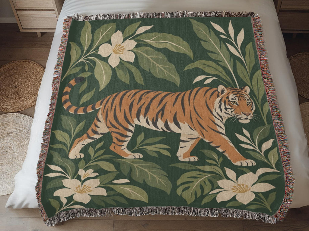 Closer view of the Tiger Botanical woven cotton blanket laid on a bed: the whole striding tiger among forest-green leaves and cream blossoms, with fringe.