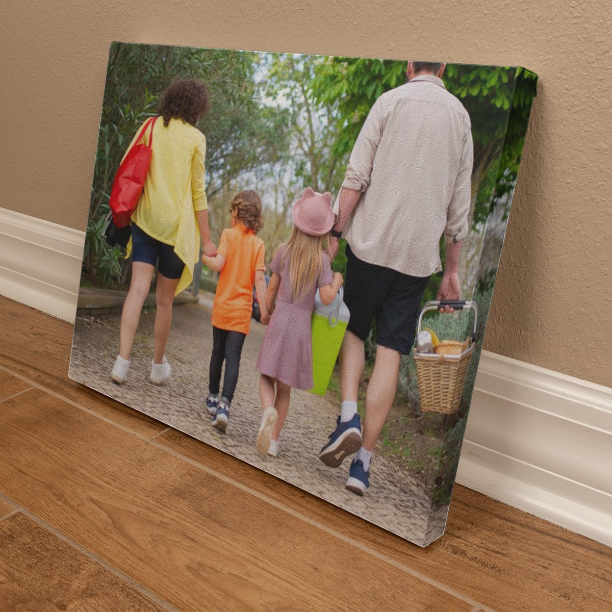 Angled view of the family portrait canvas resting on a wood floor against a baseboard, showing the wrapped side edge and the picture continuing around it.