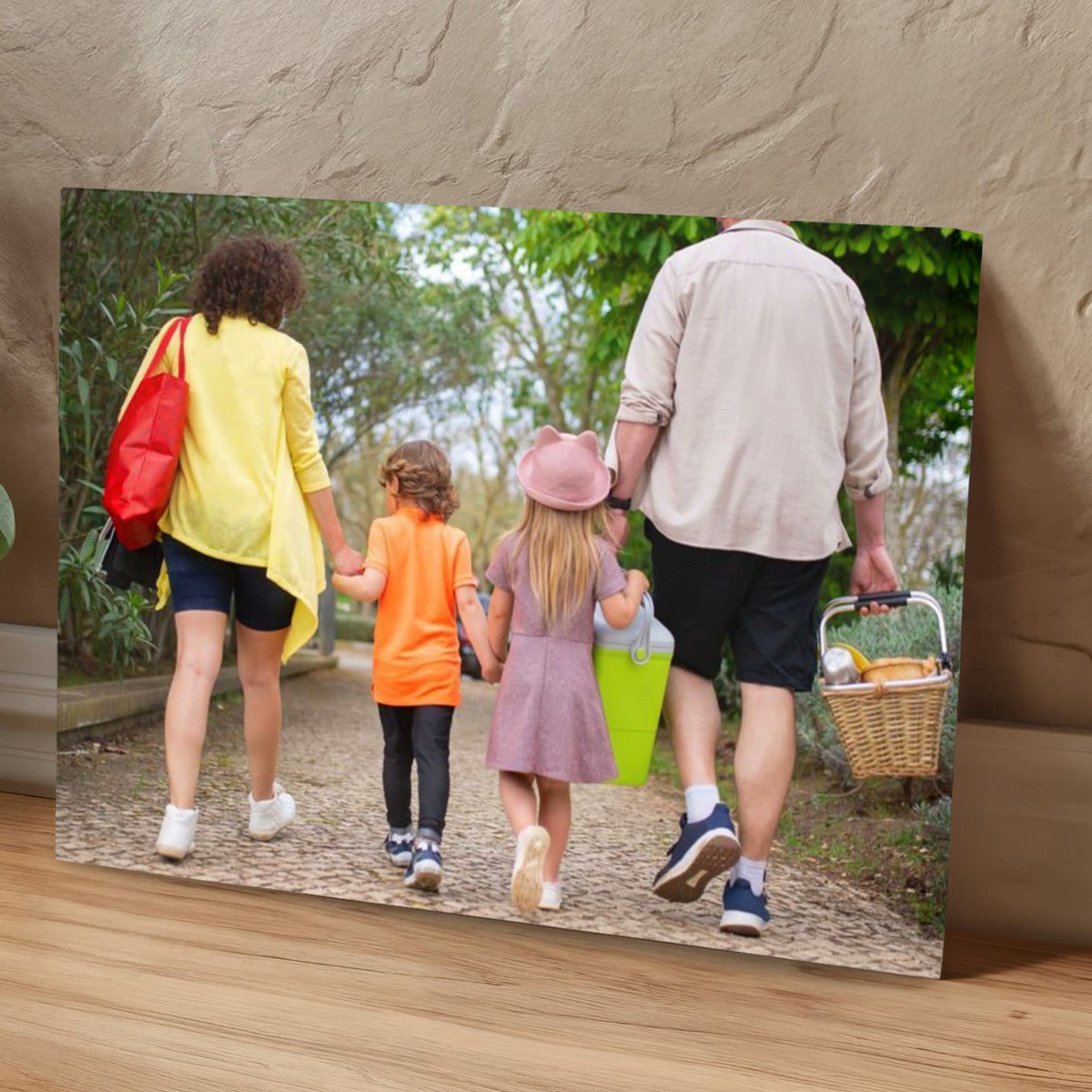 Custom photo canvas of a family on a park walk, propped against a textured plaster wall next to a green houseplant in a calm room.